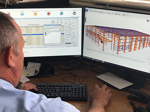 Waring Buildings employee sat at computer, Tekla PowerFab shown on two computer monitors