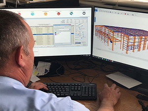 Waring Buildings employee sat at computer, Tekla PowerFab shown on two computer monitors